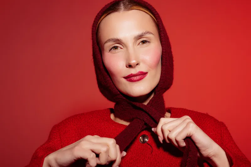 Portrait of a woman in red sweater and scarf on red background. She looks confident with natural makeup and soft lighting. Concept of fashion and style.