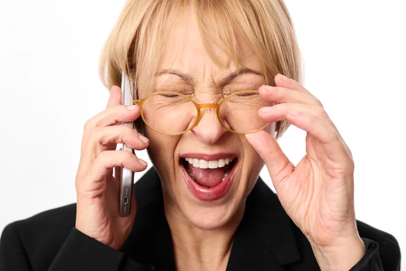 Happy woman adjusting eyewear glasses while talking on smartphone phone, smile and laughter with eyes closed, hands near face, studio background, communication and technology