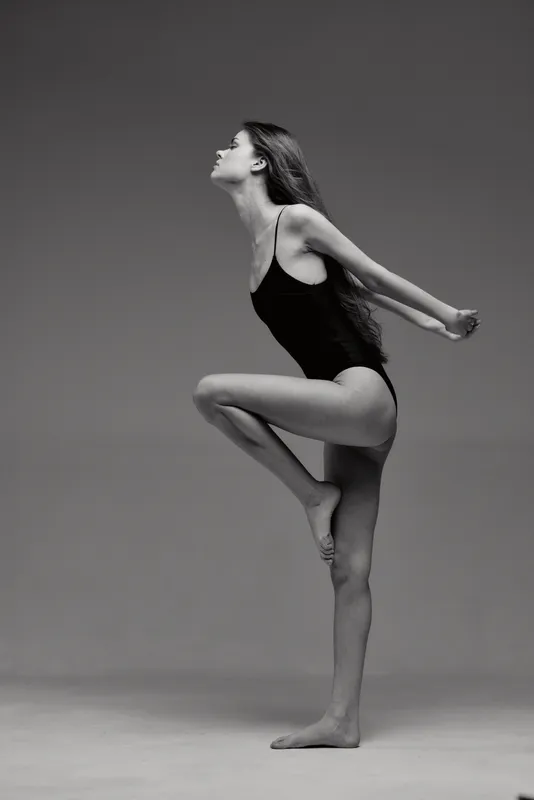 Black and white artistic photo of a woman dancing in leotard, showing grace, balance, and flexibility in a studio setting.