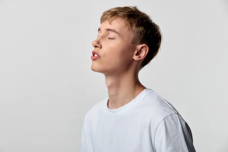 Calm man with closed eyes in a serene pose wearing a white shirt in a studio, illustrating meditation, contemplation, minimalism, stillness, relaxed mood and quiet concentration.