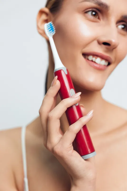 Woman toothbrush brushing hygiene electric smile oral care dental routine, close up face and hand holding red electric brush, clean fresh bathroom feel, soft light, smooth skin