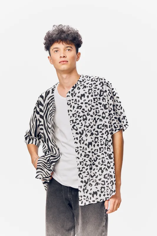 young man wearing half zebra half leopard print shirt and white t-shirt, standing against white background with serious expression, casual urban style