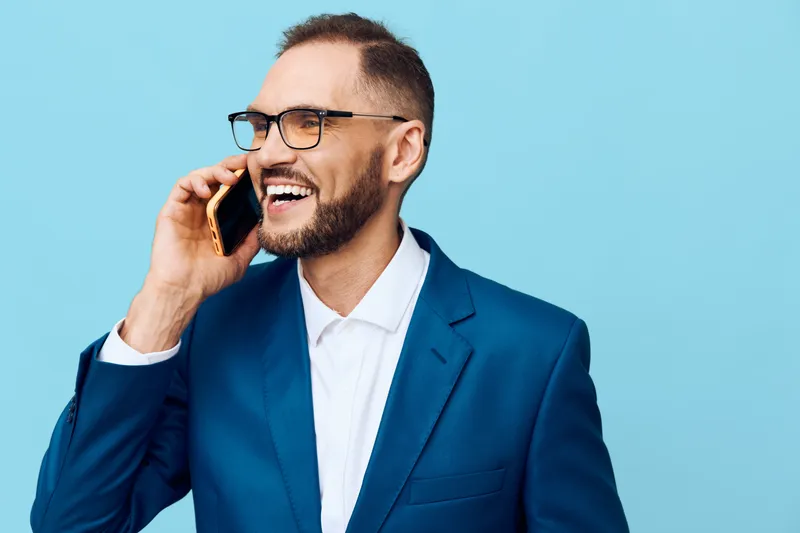 A professional man in a blue suit talks on a mobile phone, radiating confident energy. A bright colored background isolates the subject with a modern corporate vibe.