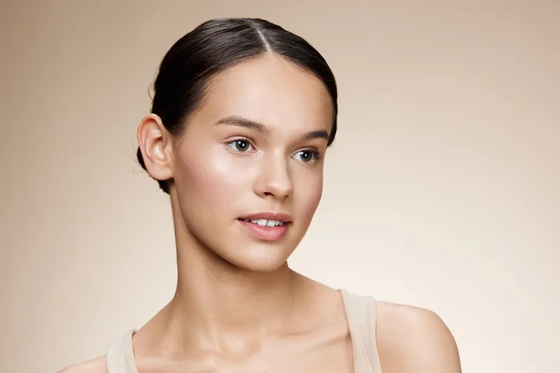 Natural beauty portrait of a young model with a soft expression, wearing minimalist makeup and a beige top, showcasing a serene and elegant look