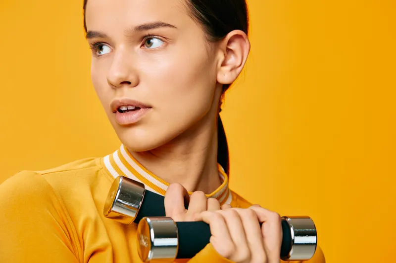Woman fitness athlete lifting dumbbells in a bright orange studio, showcasing strength, workout routine and focus during training in a modern gym setting.