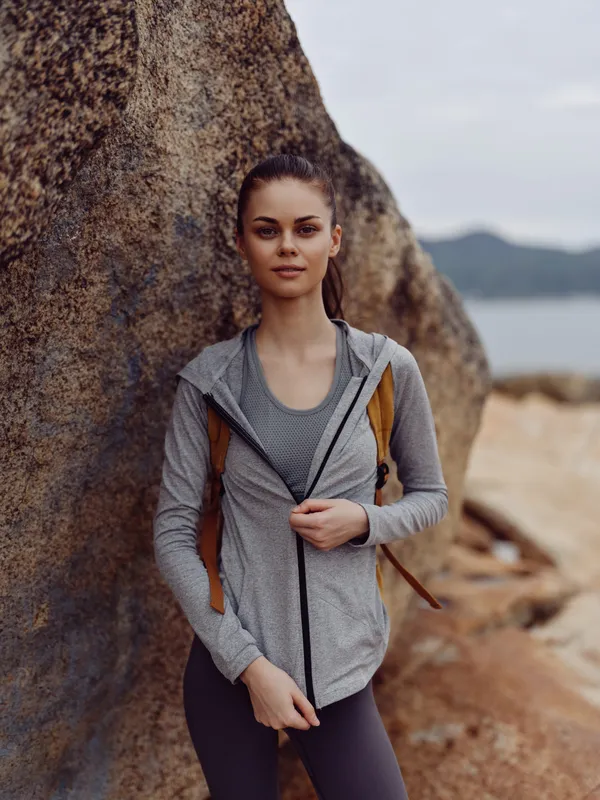 Young athletic woman in stylish sportswear standing by a rock, expressing confidence and motivation for outdoor activities in a natural setting