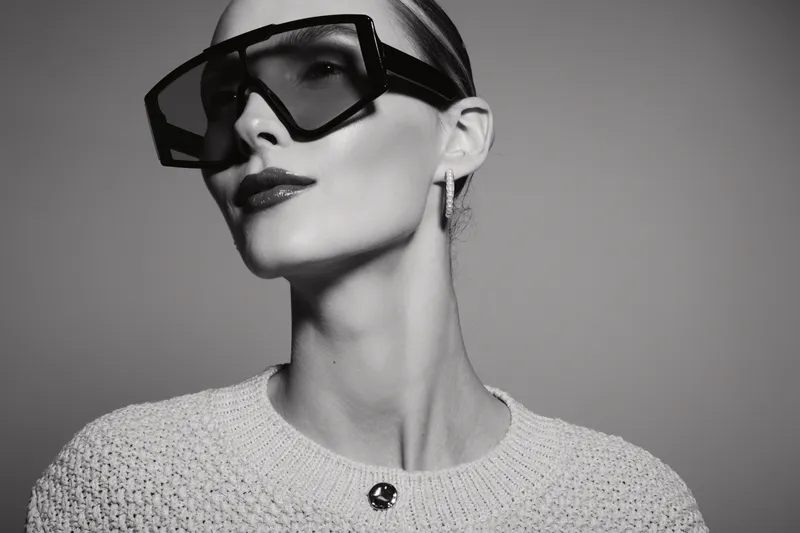 Fashionable white woman with pale skin wears large dark sunglasses and a knitted sweater. Studio portrait in black and white with elegant and modern style concept.