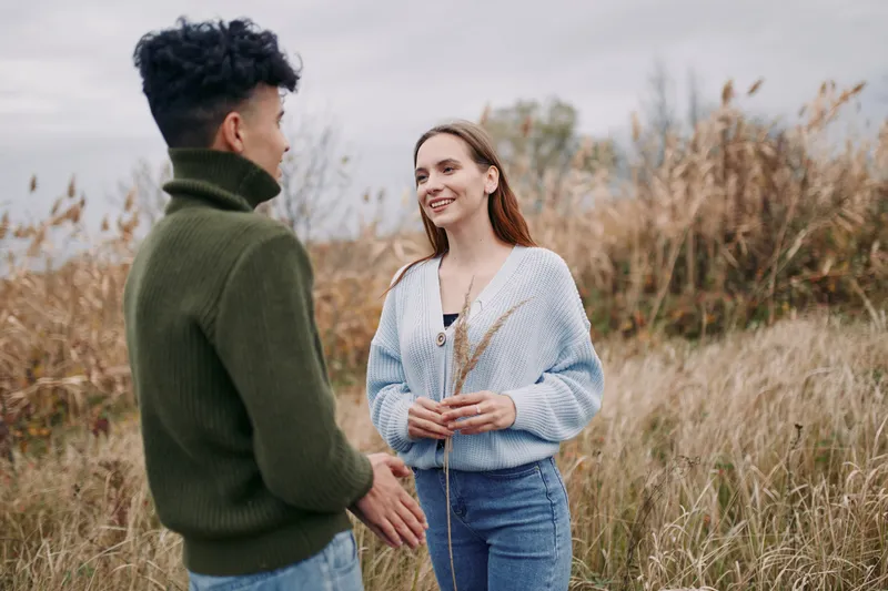 Genuine candid portrait of a young couple sharing a sincere moment in a windswept meadow, natural expressions and open interaction conveying a relatable outdoor connection.