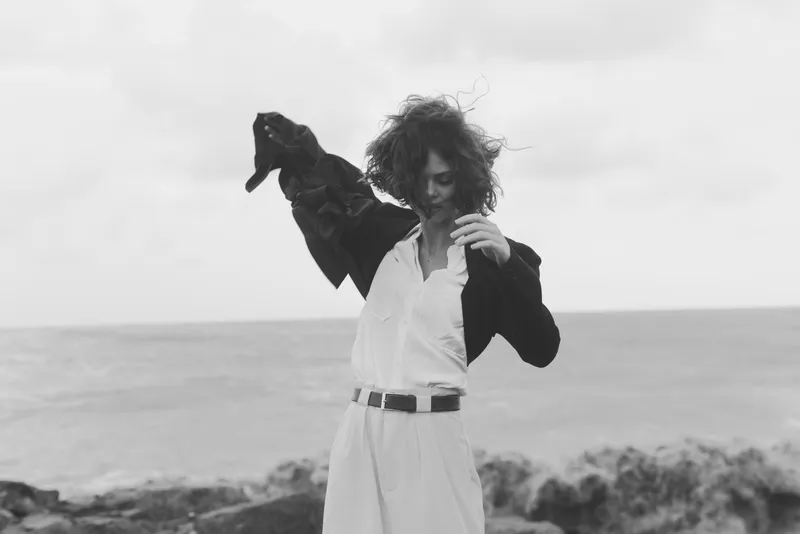 Fashion, wind, beach dress and blazer in motion with a bold silhouette, hair flowing, ocean and monochrome tones create a dramatic coastal mood and stylish, timeless appeal.