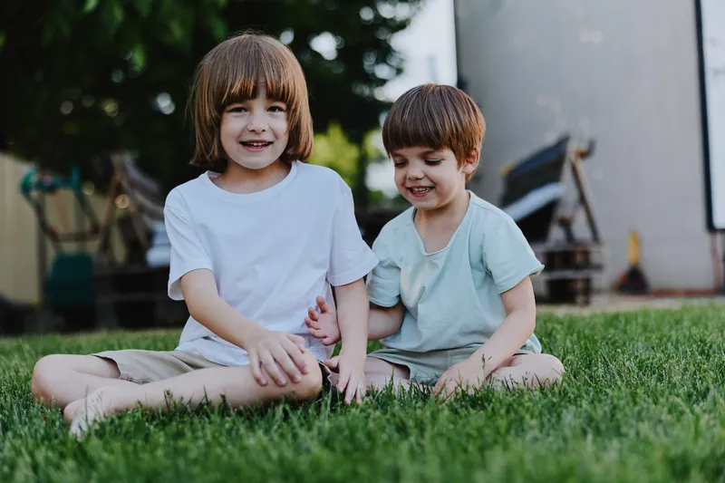 Two playful boys sitting on grass, enjoying a sunny day outdoors. Their laughter and joy create a vibrant atmosphere, perfect for family moments.