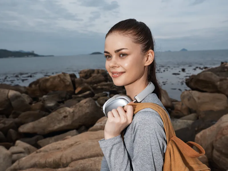 Young woman with headphones enjoying nature by the sea, showcasing a relaxed vibe and casual fashion in a serene outdoor setting