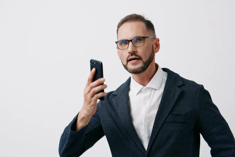A focused business professional man speaks on a mobile phone, wearing a suit, with confident posture and intense gaze against an isolated colorful background.