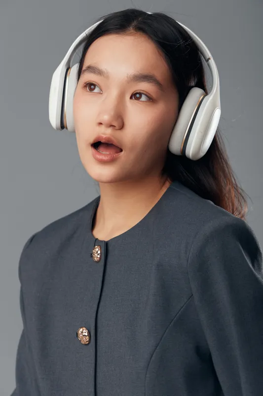 Young woman with headphones listening to music and enjoying sound with open mouth in casual outfit on neutral background. Female portrait with audio technology and entertainment concept.