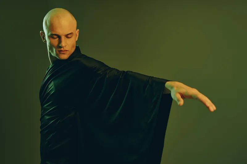 A poised man in a flowing black robe captures attention with his dramatic pose, showcasing elegance and strength. The image embodies a sense of calm and focus.