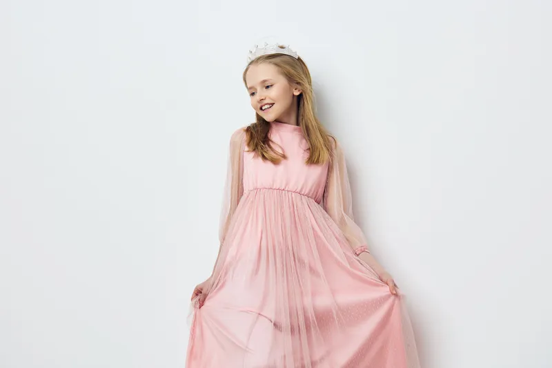 Beautiful young girl in a pink dress, exuding joy, against a minimalist white background, perfect for children s fashion and celebration concepts