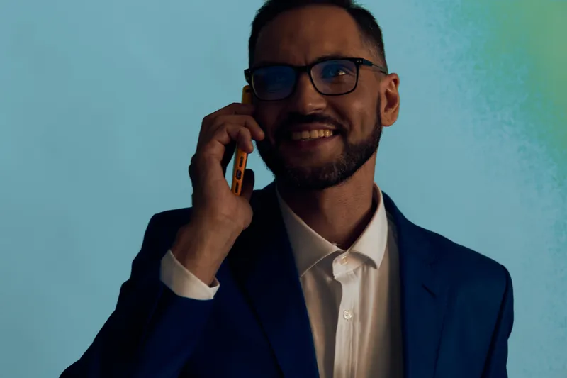 A professional male on a vibrant solid background, business subject, confident and focused, smiling softly while talking on a mobile phone, dressed in a suit for an executive look.