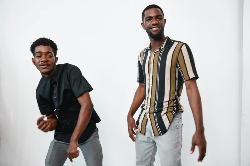 Two young black men with dark skin posing and smiling in casual clothes against white background. Male friends, fashion, lifestyle and happiness in studio portrait.