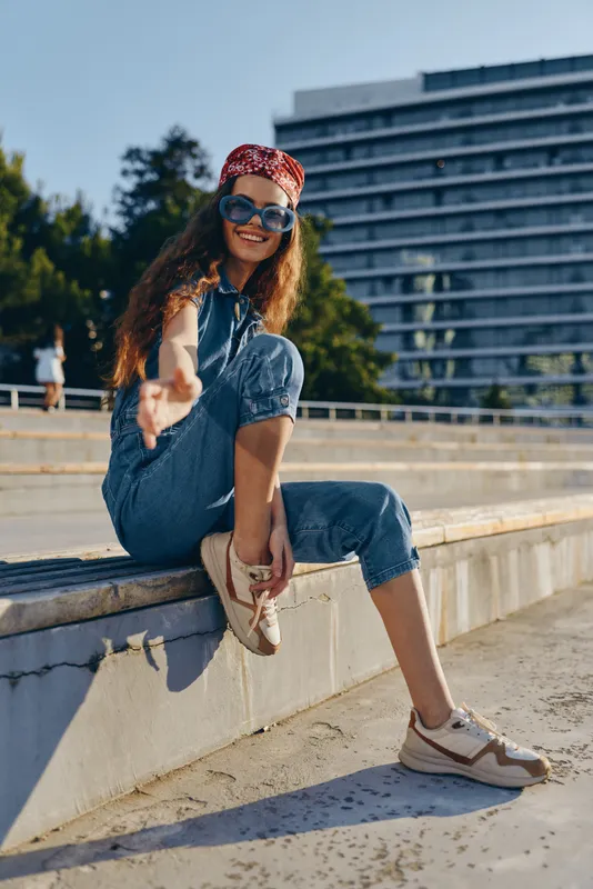 Lifestyle woman in modern boho-western denim street style wearing sunglasses and red bandana, relaxed outdoors with film color effect capturing casual urban vibe.