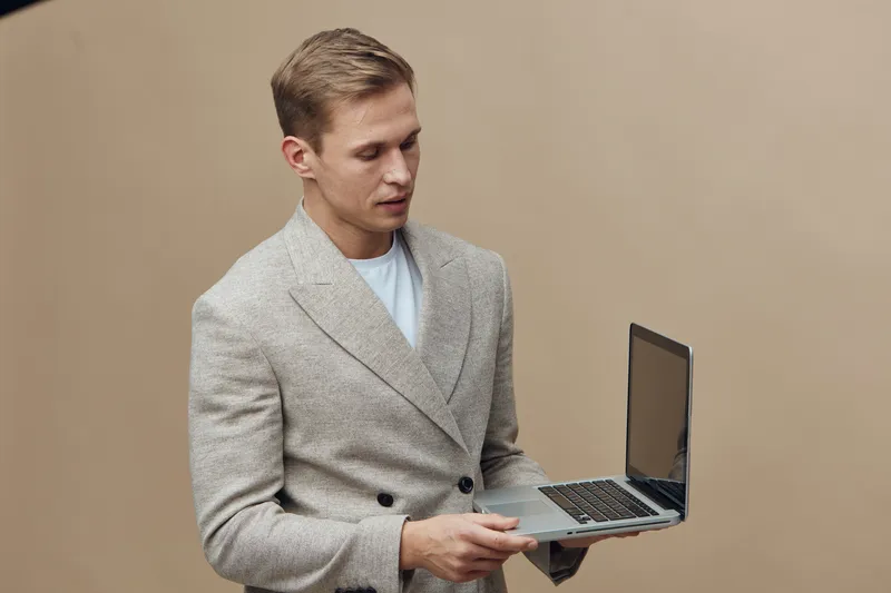 young man with laptop working on digital nomad lifestyle remote job isolated beige background casual style technology concept