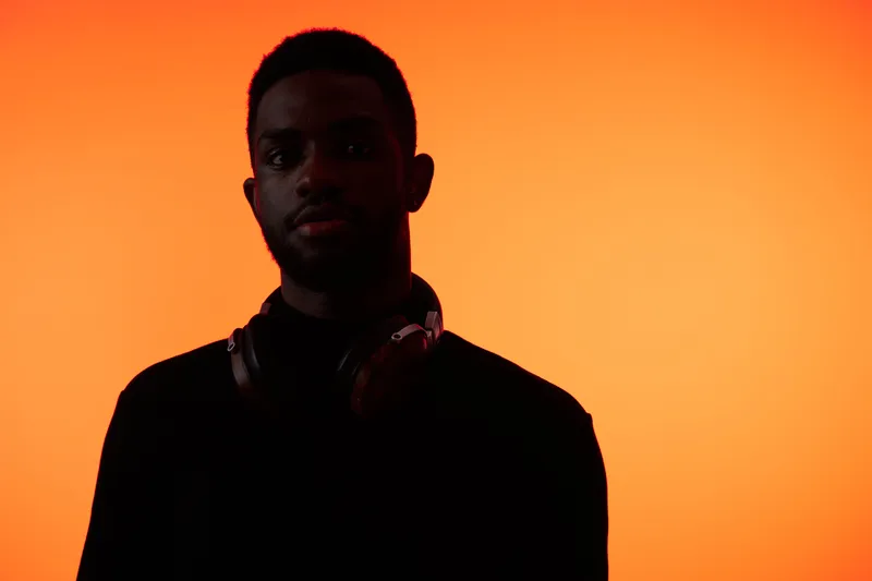 A young Black man in silhouette with headphones against a vibrant orange background, conveying a sense of music enjoyment, focus, and modern lifestyle