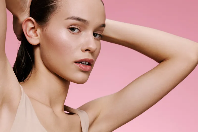 Young woman with natural makeup posing against a soft pink background, showing confidence and beauty through subtle expressions, perfect for skincare or wellness themes