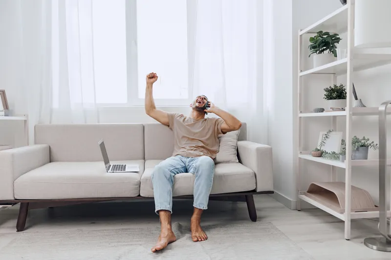 Relaxed man enjoying a refreshing drink while sitting on a cozy couch in a bright, modern living room. A perfect blend of comfort and leisure for home life.