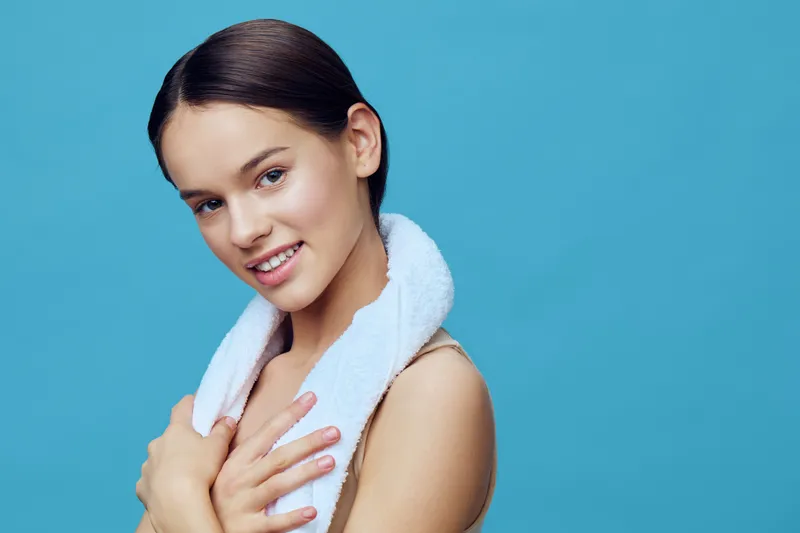 Young woman with a towel looking happily at the camera, showcasing a healthy lifestyle and clean beauty against a bright blue background