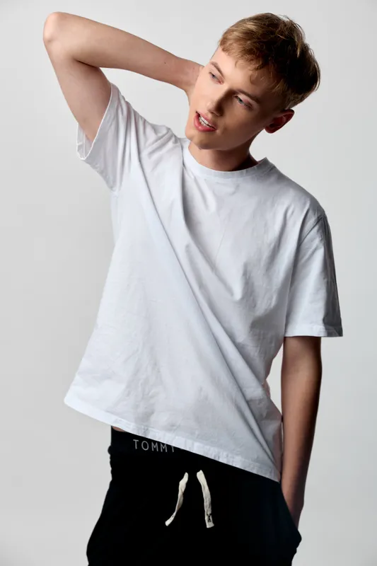 Stretching, casual youth in a white shirt with a relaxed neck pose in a clean studio, simple fashion vibe, emphasizing comfort, movement and everyday wear