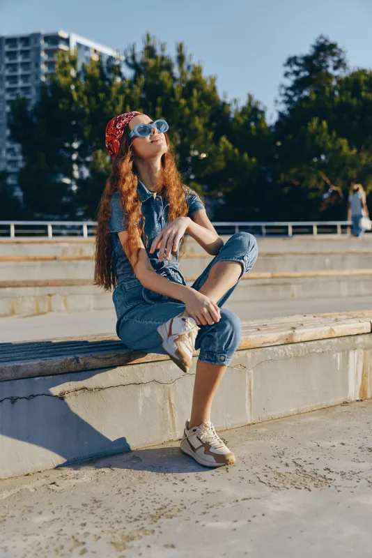 lifestyle woman in modern boho-western denim street style wearing sunglasses and red bandana, relaxed pose with film color tones in outdoor sunny urban setting