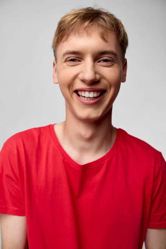 Bright studio shot of a smiling man in a red shirt conveying cheerful energy, approachable mood and casual style for lifestyle, fashion and advertising contexts, with warm lighting and a friendly