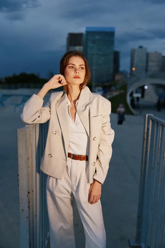 Confident woman in a stylish business outfit poses against a city skyline at dusk, embodying professionalism and elegance.