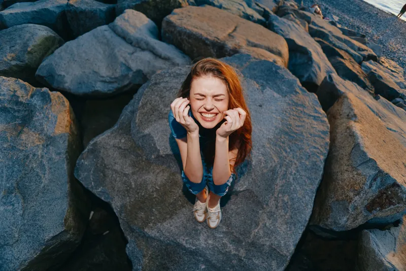 Lifestyle woman with modern boho-western denim street style laughing joyfully on large rocks in warm natural light with film color aesthetics and casual summer outfit
