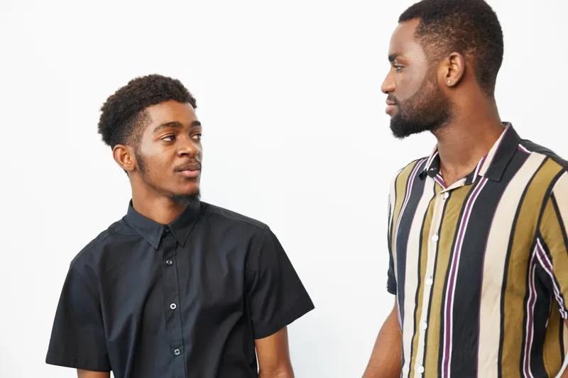 Two black men engaging in a thoughtful conversation, showcasing friendship and connection in a modern setting. Their expressions reflect a sense of understanding and camaraderie.
