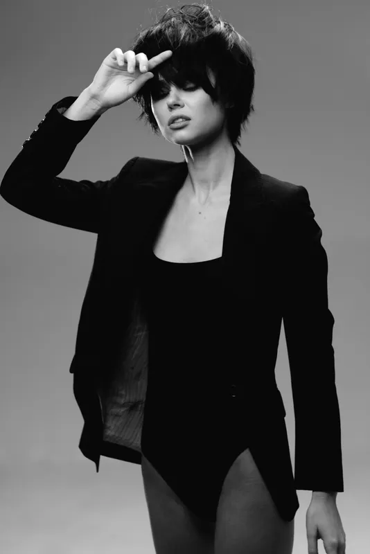 Black and white portrait of a stylish woman with short dark hair wearing a blazer expressing confidence and elegance.