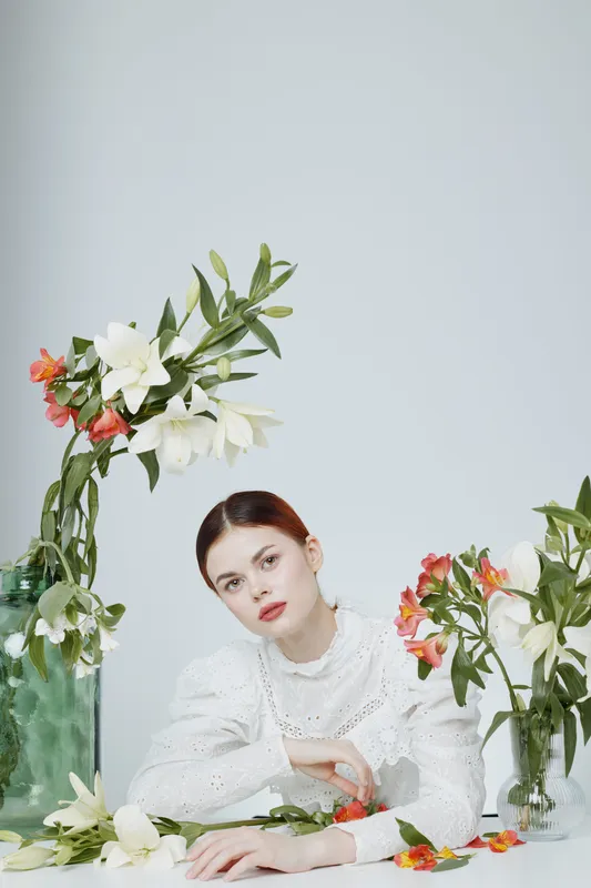 Elegant young woman in a white blouse surrounded by colorful flowers, capturing a serene and fresh spring vibe, ideal for wellness and beauty themes