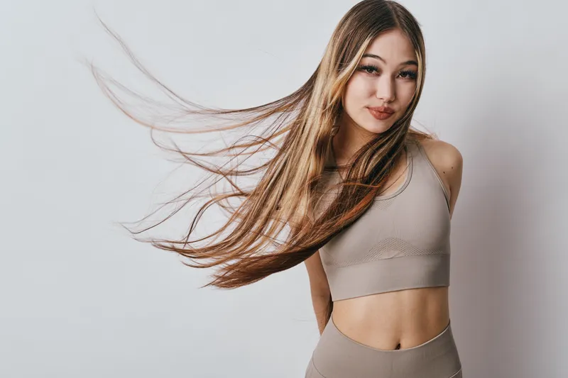 Young woman in athletic wear with long flowing hair posing on white background, fitness, healthy lifestyle, beauty, confidence, sport and casual style portrait.