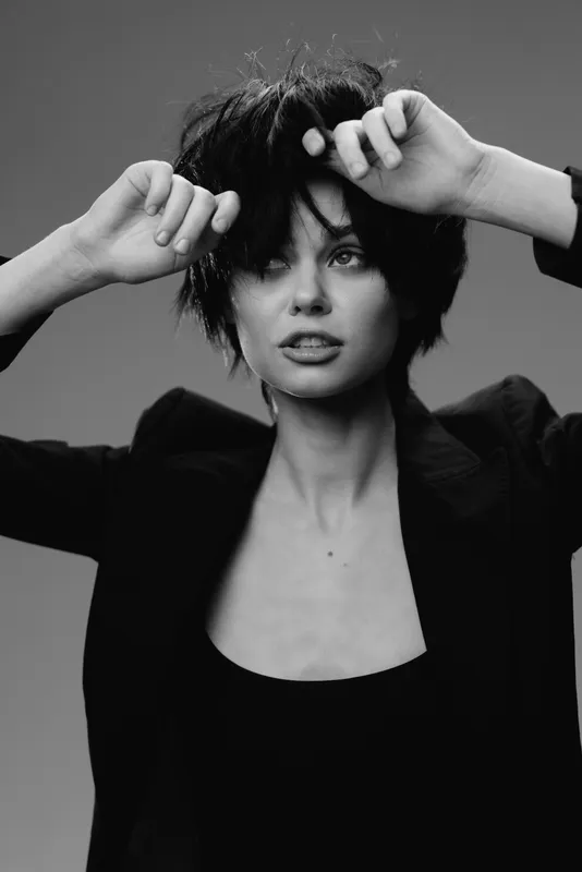 Black and white portrait of a young woman with short hair wearing a blazer, posing confidently with expressive hands.