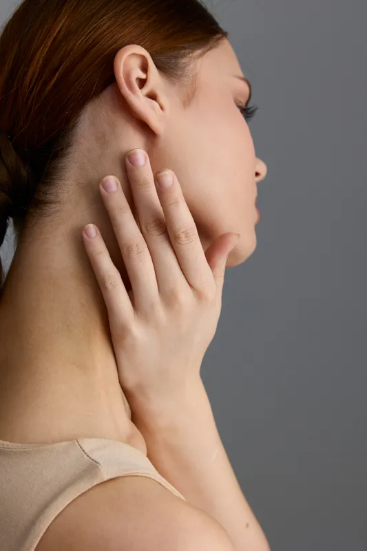 Beauty woman with smooth skin touching her neck gently, showcasing natural elegance and delicate hand pose against a soft neutral background.