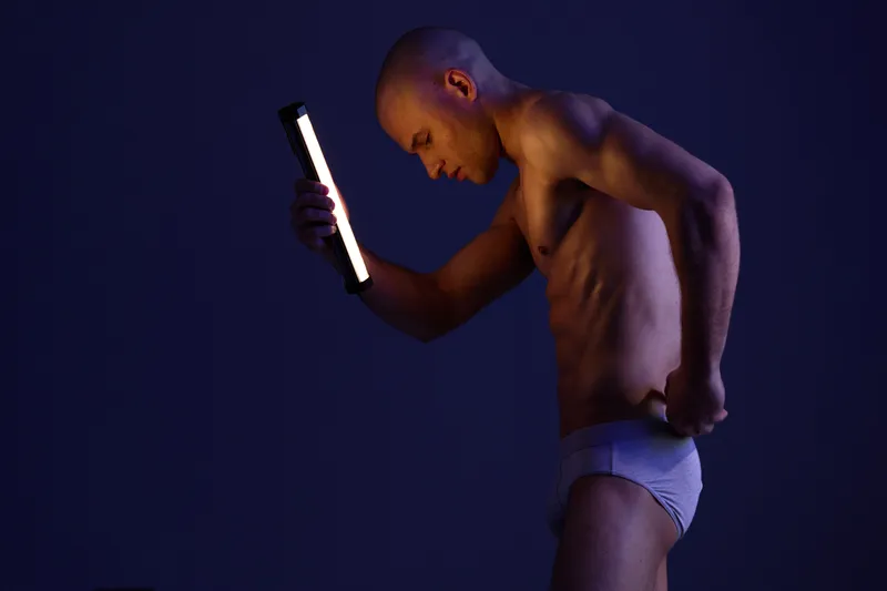 Athletic man posing with a light in a dark setting, showcasing emotion and strength. This image captures a unique moment of thoughtful expression and physicality.