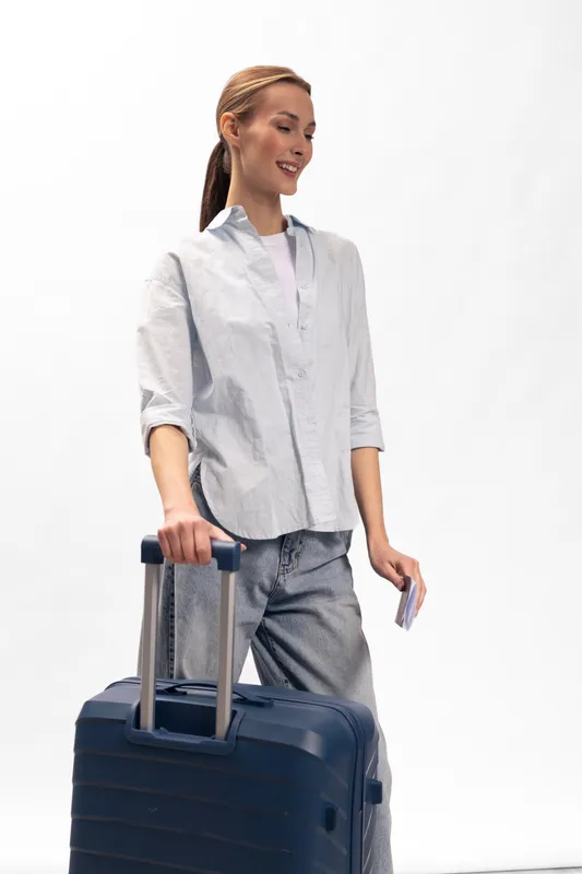 Young woman with long hair stands with a large suitcase and travel documents, smiling and wearing casual clothes. Concept of travel, vacation, tourism, and leisure activity.
