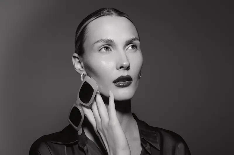 Portrait of a fair skinned Caucasian woman with slicked back hair wearing large earrings and dark lipstick. Studio lighting highlights her smooth skin and elegant pose.