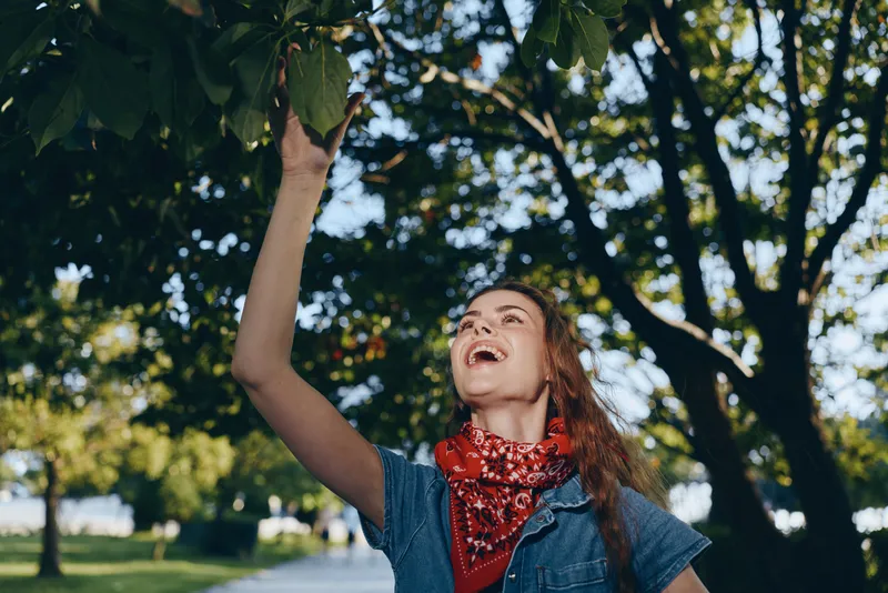 lifestyle woman in modern boho-western denim street style joyfully reaching for fruit on tree in warm natural outdoor setting film color