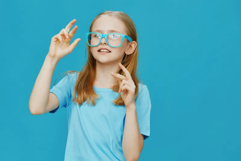 A cheerful girl with glasses in a blue t shirt posing against a vibrant blue background, showcasing a playful and imaginative spirit
