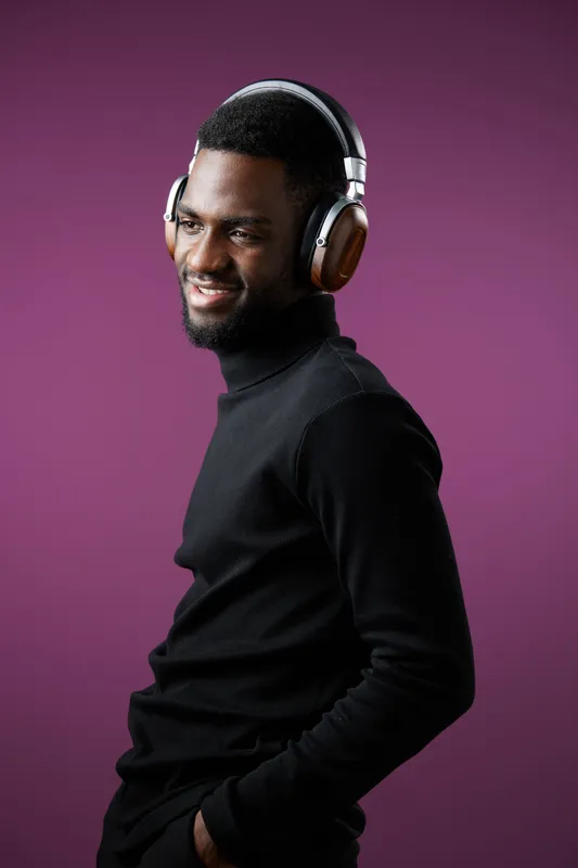 Young African man with headphones wearing a black turtleneck sweater, smiling against a purple background, perfect for music or lifestyle concepts