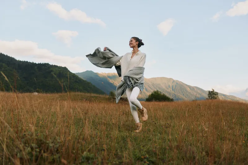 Young woman runs across a golden field with mountains in the distance, expressing carefree joy in a bright outdoor moment