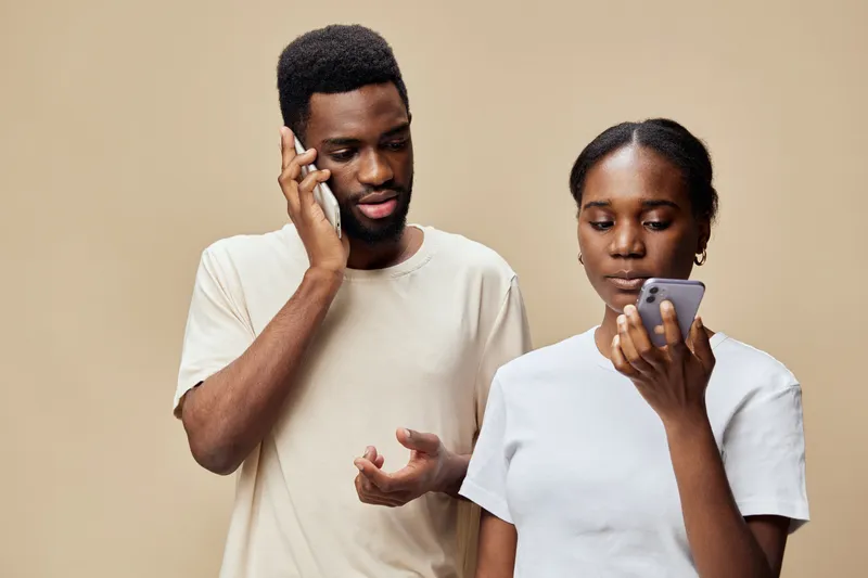 A young African couple engaged in a conversation, showcasing modern communication with smartphones against a neutral background