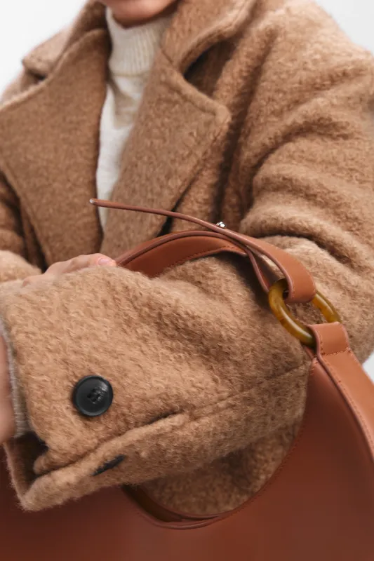 asian woman wearing a cozy brown coat with a stylish handbag, posing in a minimalist setting. she exudes confidence and warmth, illustrating contemporary fashion and everyday elegance.