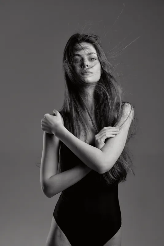 Black and white portrait of a woman with long hair embracing herself, emotive and artistic mood.