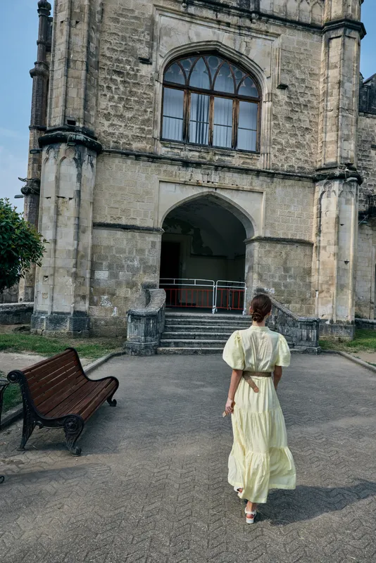 Woman walking toward historic stone architecture in courtyard, back view with flowing dress, travel mood, authenticity and inclusivity in natural urban heritage scene