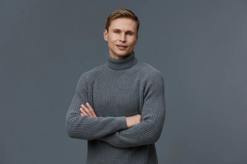 Full body smiling happy cheerful young caucasian man wearing gray knitted turtleneck sweater looking at camera holding his arms crossed isolated on plain gray background studio portrait. People lifest